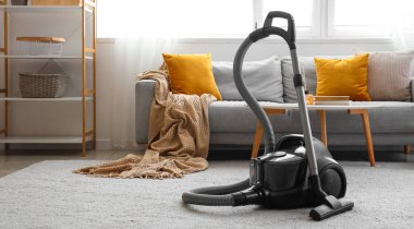 Elektrikli süpürgesi, kanepesi ve masası olan aydınlık oturma odasının içinde.