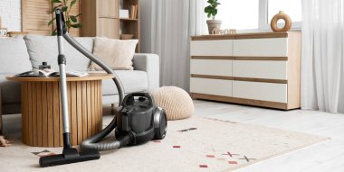 Oturma odasında elektrikli süpürge, masa ve kanepe var.