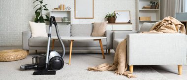 Oturma odasının içinde elektrikli süpürge, kanepe ve masa var.