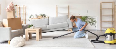 Kanepenin altını süpürge ile temizleyen erkek hademe.