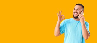 Mutlu genç adam telefonla konuşuyor ve sarı arkaplanda mesaj için yeri olan bir jest gösteriyor.