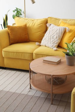 Oturma odasındaki rahat sarı kanepenin yanında saksısı ve kitabı olan kahve masası.