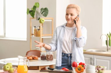 Elmalı genç bir kadın mutfakta cep telefonuyla konuşuyor.