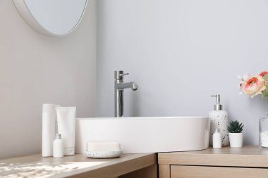 Lavabo, banyo aksesuarları ve ranunculus çiçekleri hafif banyodaki ahşap dolapta.