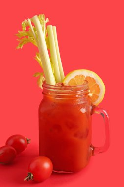 Kırmızı zemin üzerinde kereviz ve limon olan bir kavanoz Bloody Mary.