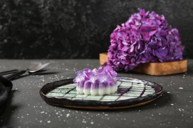 Siyah masa üzerinde güzel ortanca çiçekleri olan bir tabak panna cotta.