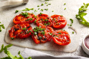 Lezzetli ızgara domatesli tahta ve gri arka planda yeşil soğan.