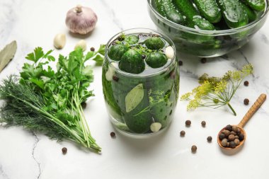 Taze salatalıklı kavanoz ve beyaz mermer arka planda korunması için malzemeler.