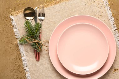 Pembe tabaklar, çatal bıçak takımı ve kahverengi arka planda köknar ağacı dalı olan Noel sofrası.