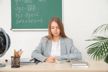 Genç matematik öğretmeni sınıftaki tahta masada öğrencinin ödevlerini kontrol ediyor.