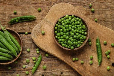 Ahşap zemin üzerinde taze bezelyeler olan kâseler ve yiyecekler.