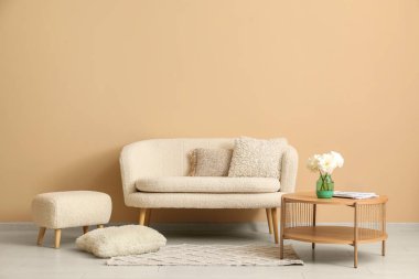 Tahta sehpa, kanepe ve bej duvarın yanında yastıklar.