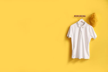 Sarı arka planda asılı şık beyaz tişört ve şapka