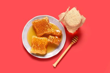 Kavanoz dolusu tatlı bal ve kırmızı arka planda taraklı tabak