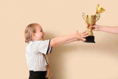 Bej arka planda altın kupalar alan mutlu küçük okul kızı.