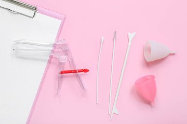 Pembe arka planda jinekolojik spekulum, regl bardakları ve pap smear test araçlarıyla pano