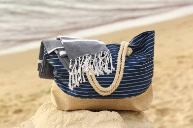 Okyanus kıyısında üzerinde plaj battaniyesi olan bir yaz çantası.