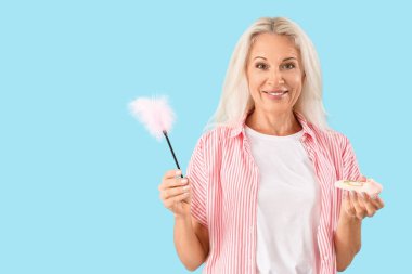 Mavi arka planda tüy çubuğu ve vibratörü olan olgun bir kadın.