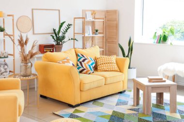 Sarı kanepe ve masalarla aydınlık oturma odasının içinde.