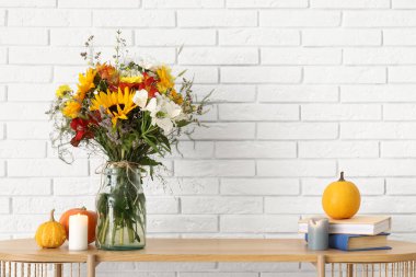 Raflarda bir buket sonbahar çiçeği ve beyaz tuğla duvarın yanında dekor var.