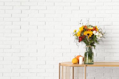 Raflarda bir buket sonbahar çiçeği ve beyaz tuğla duvarın yanında dekor var.