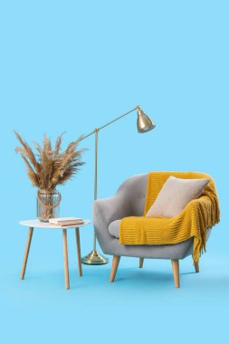 Yastıklı rahat gri koltuk, sıcak battaniye ve kahve masasında mavi arka planda otlar.