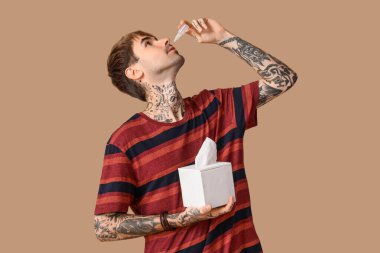 Kahverengi arka planda burun damlası ve dokuları olan alerjik genç bir adam.