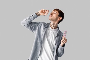 Gri arka planda burun damlası kullanan alerjik genç adam.