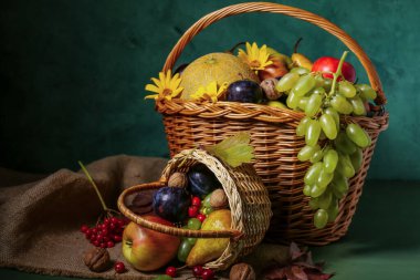 Yeşil duvarın yanındaki masada farklı taze meyvelerle dolu sepetler.