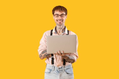 Sarı arka planda modern dizüstü bilgisayarı olan mutlu genç adam.