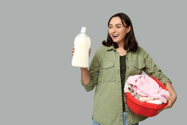 Çamaşır sepeti ve gri arka planda bir şişe deterjanı olan genç bir kadın.