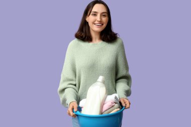 Çamaşır sepeti ve leylak arka planda bir şişe deterjanı olan genç bir kadın.