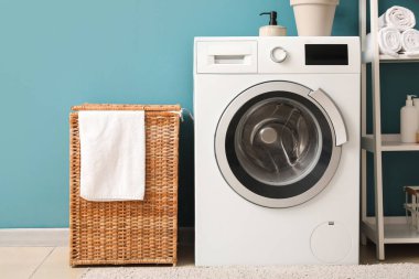Çamaşır odasındaki mavi duvarın yanında sepet ve çamaşır makinesi.