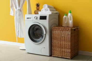 Çamaşır odasının içinde hasır sepeti, çamaşır makinesi ve bornoz var.
