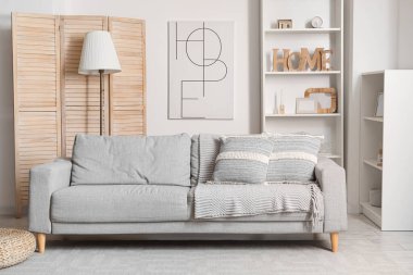 Gri kanepe, lamba ve raf üniteleriyle modern oturma odasının içinde.