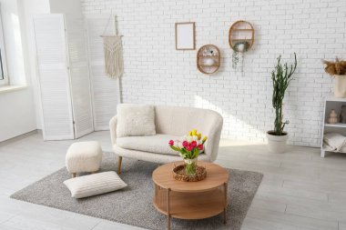 Beyaz çatı katı tarzı oturma odasının içinde kanepe, çiçekler ve kahve masası var.