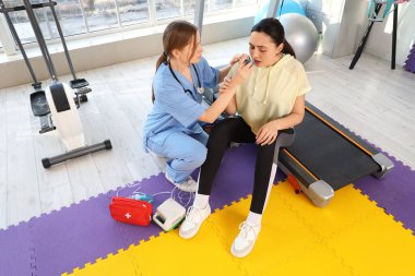 Spreyli kadın doktor jimnastik salonunda genç bir kadına ilk yardım yapıyor.