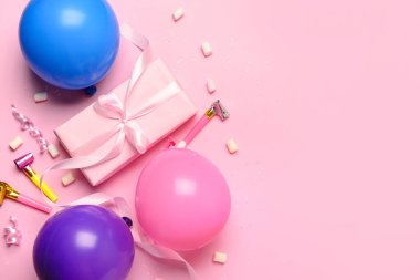 Hediye kutusu, balonlar ve pembe arka planda parti kornaları.