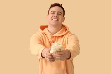 Genç adam gülümsüyor ve bej arka planda lezzetli bir donör kebabı tutuyor.