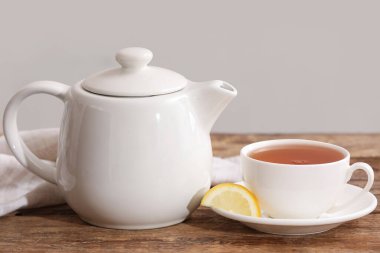 Bir fincan sıcak çay, çaydanlık ve bej duvarın yanındaki ahşap masada kumaş peçete.