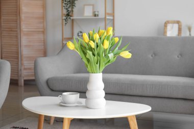 Masasında laleler ve oturma odasında bir fincan çay olan güzel bir vazo.