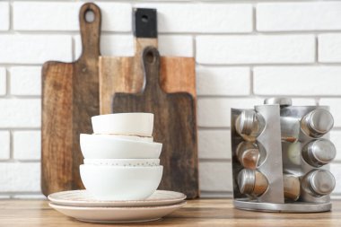 Beyaz tuğla duvarın yanındaki ahşap masada yığınla temiz sofra takımı var.