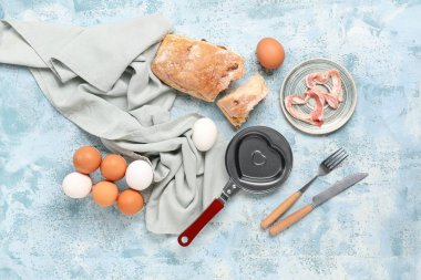 Mavi arka planda kalp şeklinde kızartma tavası, peçete, çatal bıçak ve yumurta kompozisyonu