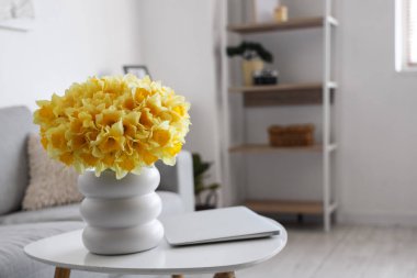 Oturma odasındaki masada nergis ve dizüstü bilgisayarlı vazo, yakın plan.