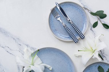 Güzel kompozisyon mavi temiz tabaklar, çiçekler ve mermer masa üzerinde çatal bıçak