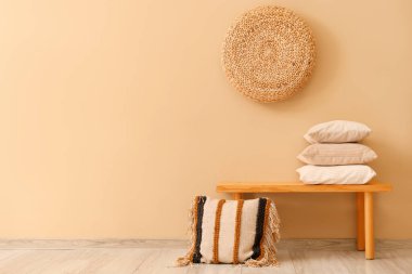 Bej duvarın yanında bir yığın yastıklı ahşap bank.