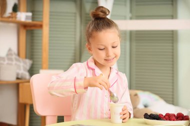 Yatak odasındaki masada pijamalı, yoğurtlu tatlı bir kız.