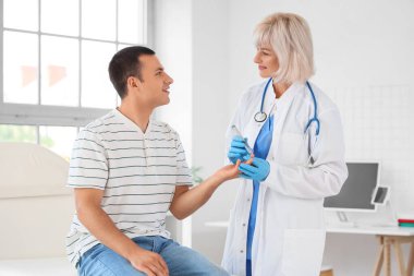 Kadın endokrinolog elinde tükenmez kalemle klinikteki kanepede kan şekeri seviyesini ölçüyor.