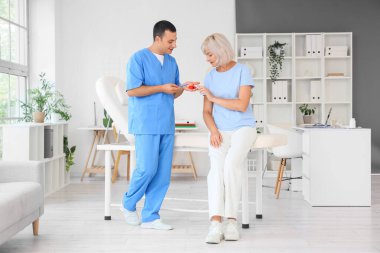 Erkek endokrinolog, klinikte olgun bir kadına tiroit bezi modeli gösteriyor.