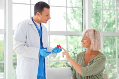 Erkek endokrinolog, klinikte olgun bir kadına tiroit bezi modeli gösteriyor.